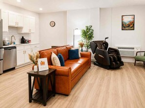 A modern living room with a leather sofa, a massage chair, a small table with a framed picture, and a kitchen in the background. - Downtown! Walk to 4th Street Live, Brown Theater (Louisville)