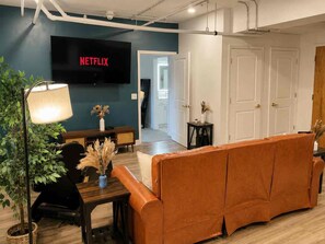 A living room with a sofa, a TV mounted on the wall, a lamp, and a plant. - Downtown! Walk to 4th Street Live, Brown Theater (Louisville)