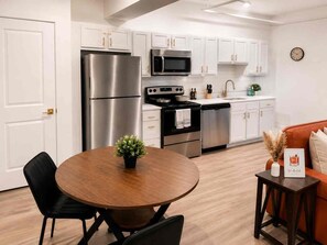 A modern kitchen with stainless steel appliances, white cabinetry, and a round dining table with chairs. - Downtown! Walk to 4th Street Live, Brown Theater (Louisville)