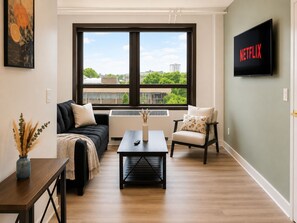 A living room with a sofa, armchair, coffee table, and a TV mounted on the wall. - Downtown! 4th Street, Brown Theatre, KFC Yum! (Louisville)