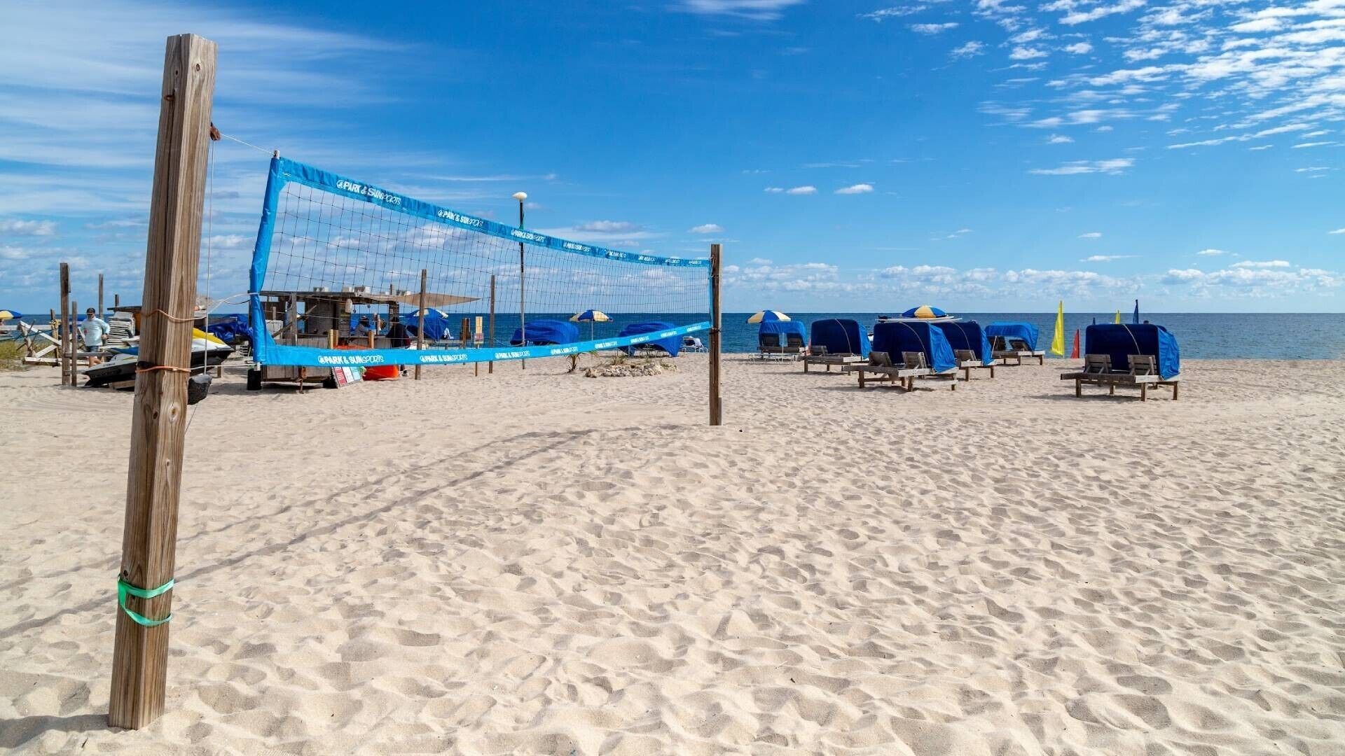Ein Beachvolleyballfeld mit blauem Netz, Liegestühlen und Sonnenschirmen.