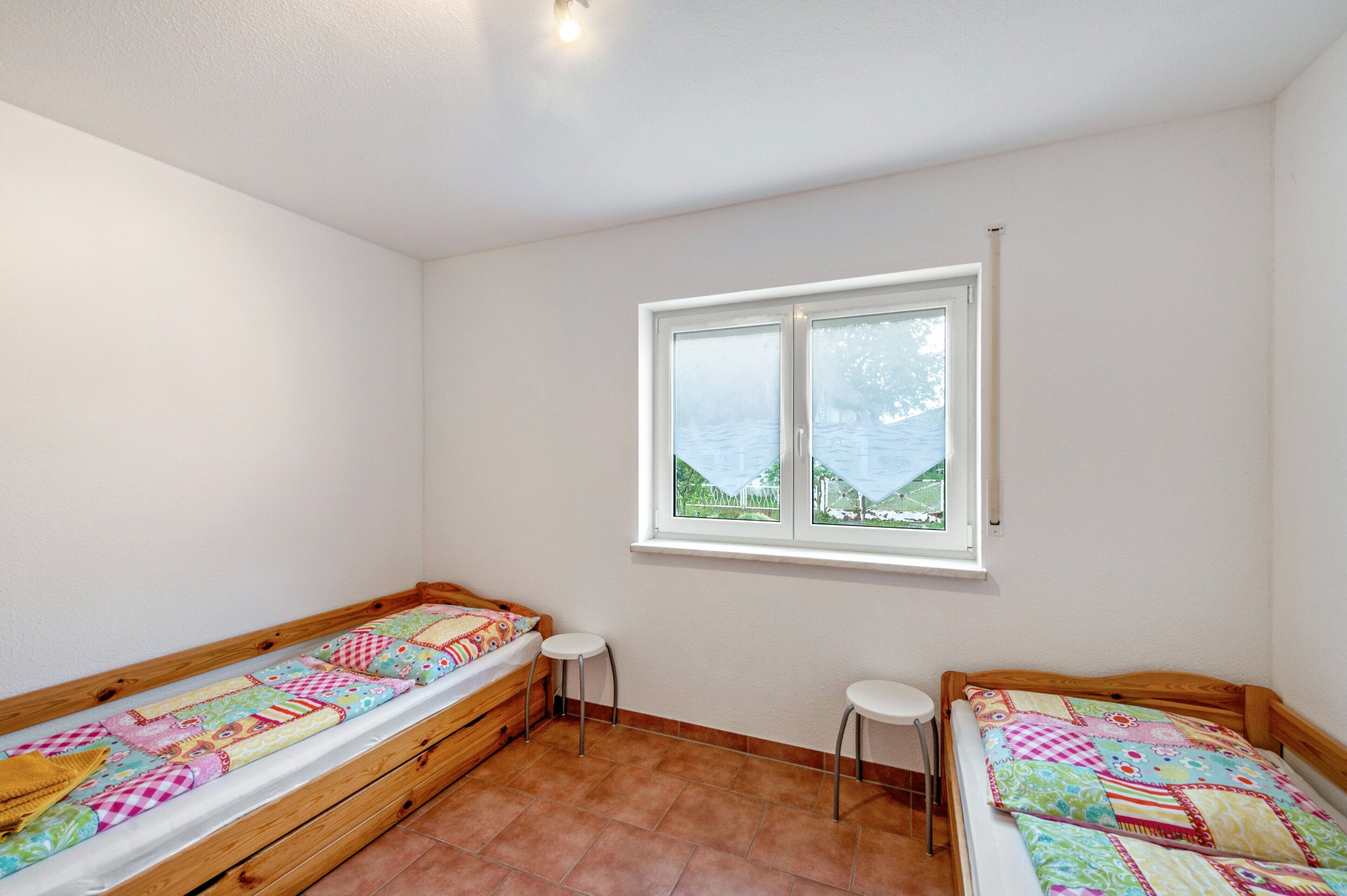 Una habitación con dos camas individuales, una ventana con vistas y un pequeño taburete.