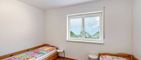Una habitación con dos camas individuales, una ventana con vistas y un pequeño taburete.