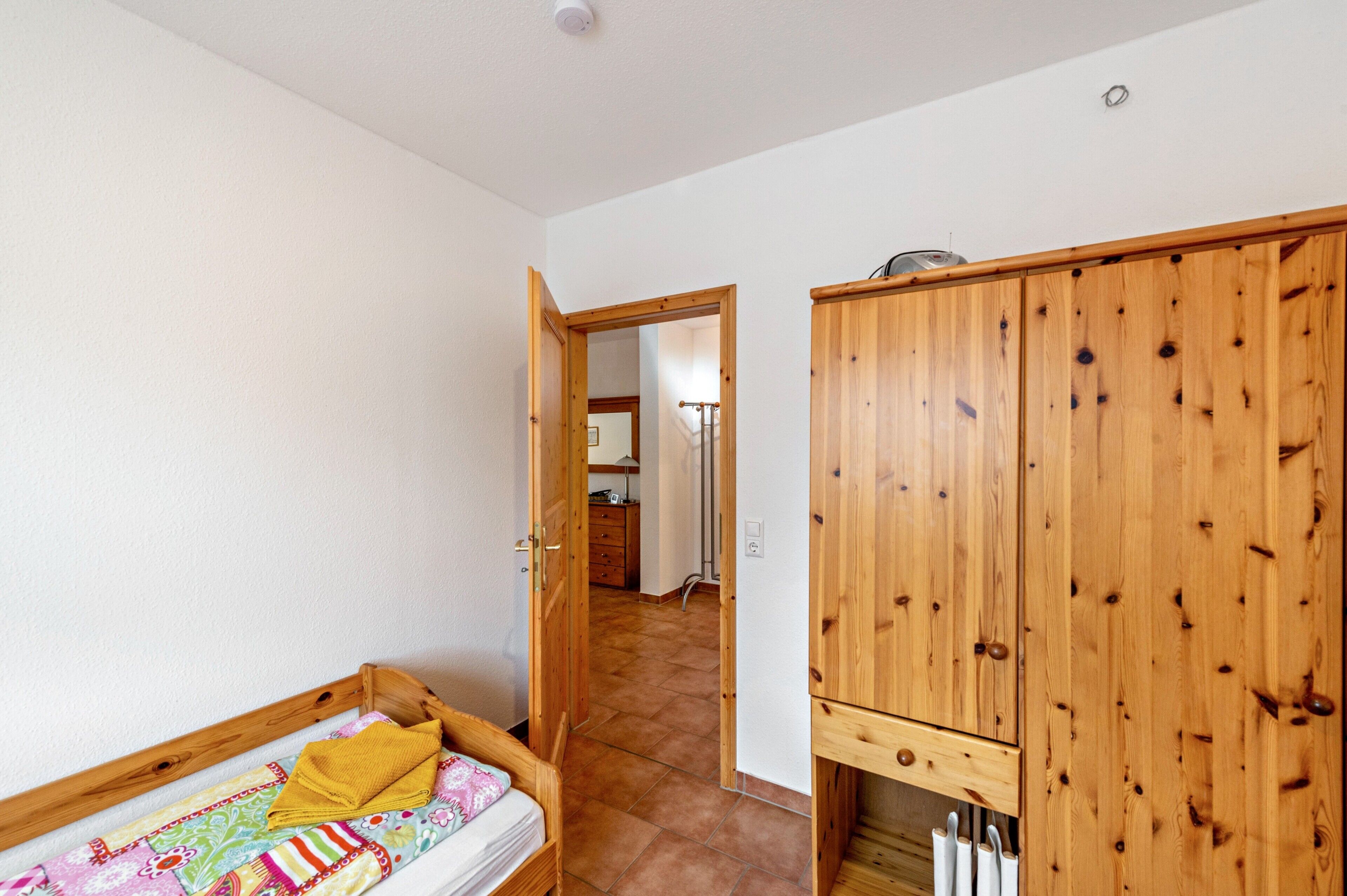 Un dormitorio con un armario de madera, una cama con una colcha colorida y un baño visible a través de una puerta abierta.
