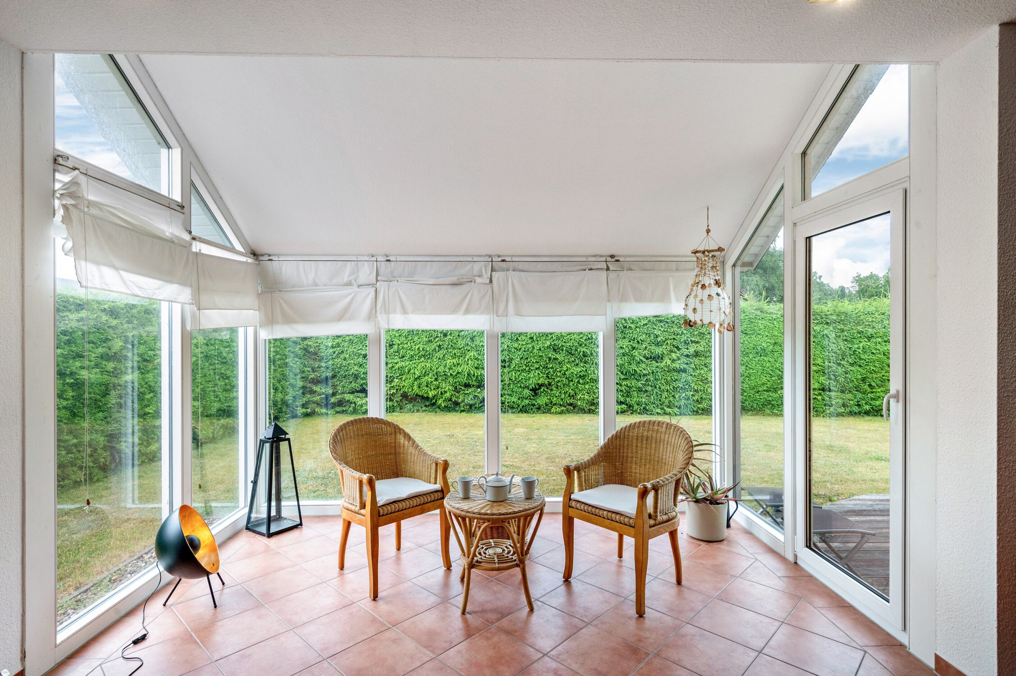 Une terrasse couverte avec des fauteuils en osier, une petite table et un luminaire suspendu.