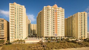 Ein Hochhaus mit mehreren Balkonen, einer zentralen Treppe und einer Strandlage.