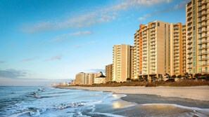 A beachfront hotel with multiple high-rise buildings, a sandy beach, and ocean waves.