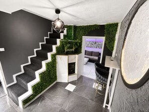 Un intĂ©rieur moderne avec un escalier noir et blanc, une cheminĂ©e et un coin salon offrant une vue sur lâextĂ©rieur.