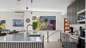 Une cuisine moderne dotée d’un grand îlot central, d’appareils électroménagers en acier inoxydable et offrant une vue sur un jardin fleuri.
