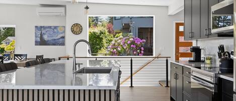A modern kitchen with a large island, stainless steel appliances, and a view of a garden with flowers.