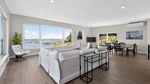 Un salon spacieux avec un grand canapé, un coin repas comprenant une table et des chaises, et une vue sur la ville grâce à de grandes fenêtres.