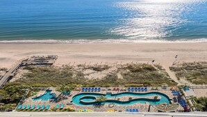 Eine Luftaufnahme eines Strandresorts mit Schwimmbad, Liegestühlen und Sandstrand.