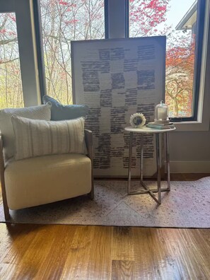 A room with a sofa, a small table with a candle, and a view of trees through large windows.