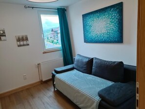 Une pièce comprenant un canapé, une fenêtre avec des rideaux, un radiateur et une œuvre d’art accrochée au mur.