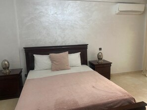 A bedroom with a bed, two nightstands, a wall-mounted air conditioner, and a textured wall. - appartement chic en plein centre (Marrakesh)