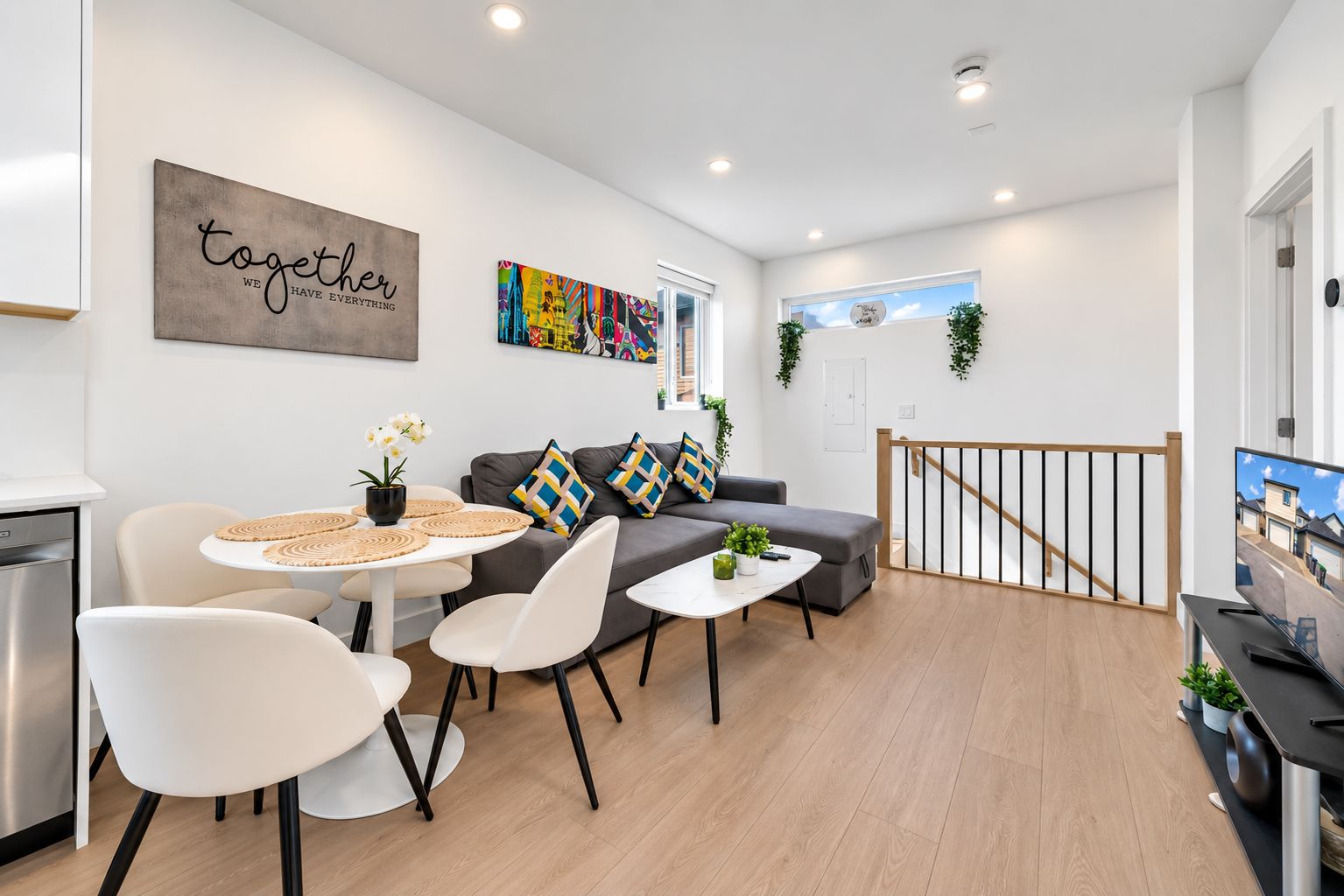 Un salón moderno con sofá, sillones, una mesa de centro y una mesa de comedor. Hay un cuadro en la pared y una ventana con vistas.