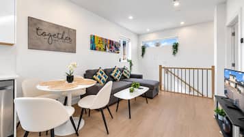 Un salón moderno con sofá, sillones, una mesa de centro y una mesa de comedor. Hay un cuadro en la pared y una ventana con vistas.