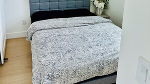 A bedroom with a bed, a headboard, a wall-mounted artwork, and a small table with a vase of flowers. - Fully AC 2 Bed 2 Bath Apartment (Surrey)