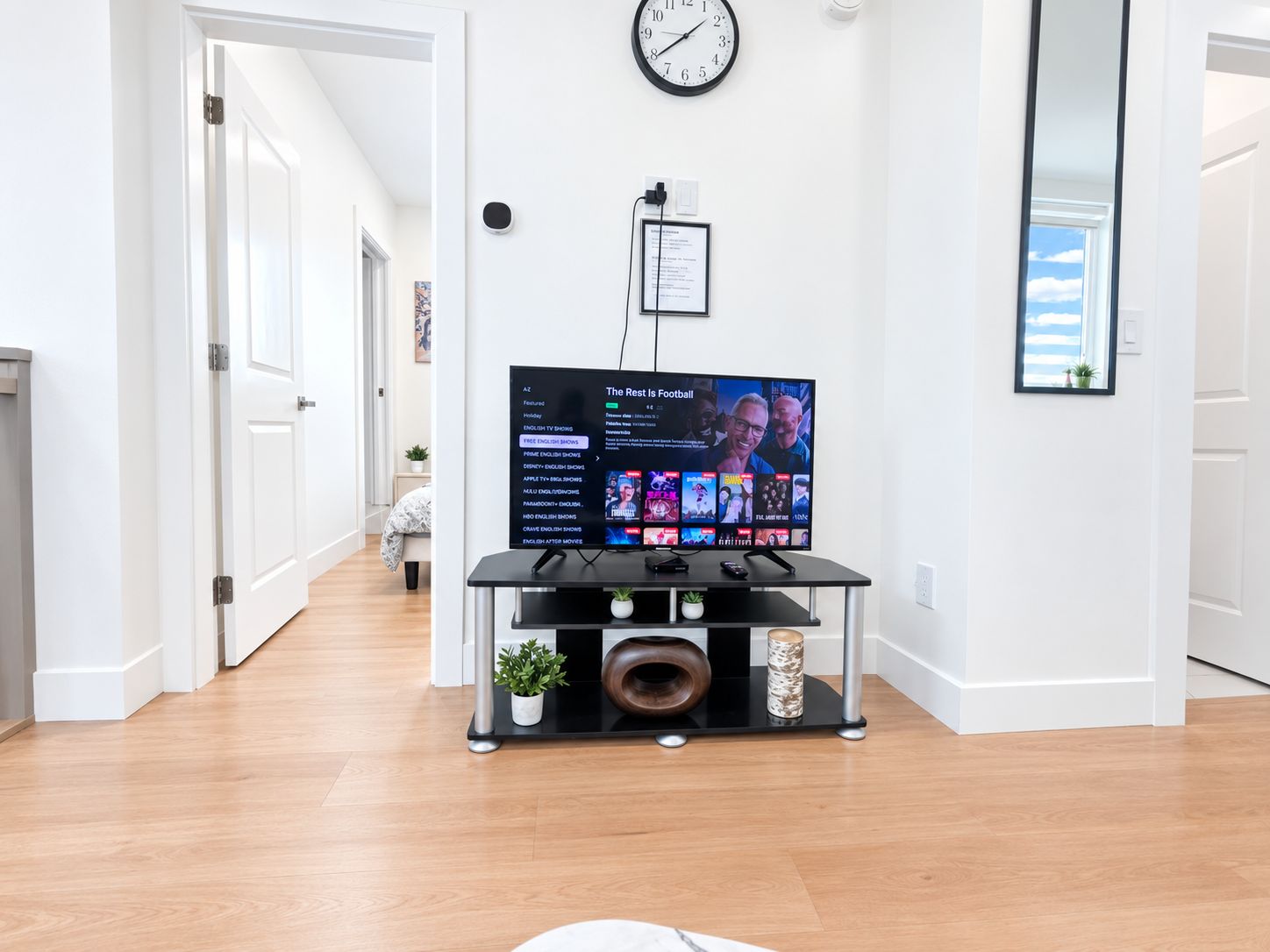Una sala de estar moderna con un televisor de pantalla plana sobre un mueble negro, un reloj de pared y un certificado en el marco en la pared.