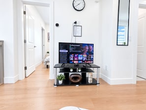 Un saló modern amb un televisor de pantalla plana sobre un suport negre, un rellotge de paret i un certificat emmarcat a la paret.