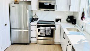 A modern kitchen with white cabinetry, stainless steel appliances, and a window. - Fully AC 2 Bed 2 Bath Apartment (Surrey)