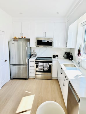 A modern kitchen with white cabinetry, stainless steel appliances, and a window. - Fully AC 2 Bed 2 Bath Apartment (Surrey)