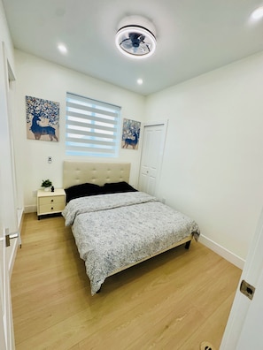 Une chambre à coucher avec un lit, des tables de chevet, un ventilateur de plafond et des œuvres d’art accrochées aux murs.