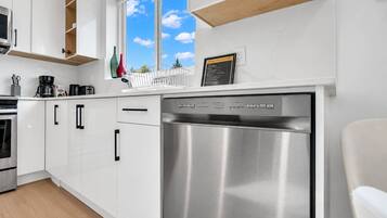Une cuisine moderne avec des meubles blancs, un lave-vaisselle en acier inoxydable et une fenêtre donnant sur le ciel.