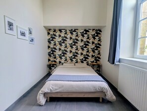 Une chambre à coucher avec un lit, un mur orné d’un motif, des tableaux encadrés, une fenêtre et un radiateur.
