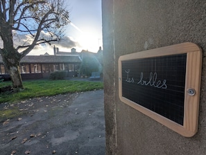 Un tableau noir sur lequel est écrit « Les billes », un arbre et, au fond, un bâtiment avec un toit en tuiles.