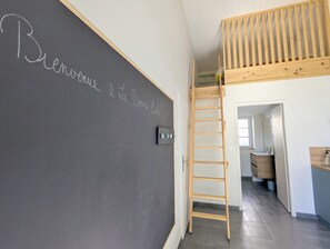 Une pièce avec un mur recouvert d’un tableau noir, une échelle en bois et une vue sur une autre pièce.