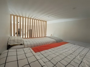 Ein Schlafzimmer mit einem Bett, einer Trennwand aus Holzleisten und Blick ins Freie.