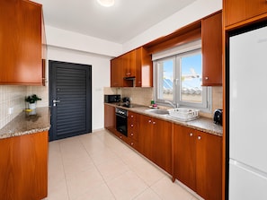 Eine Küche mit Holzausstattung, einer schwarzen Tür, einem Fenster und einem weißen Kühlschrank.