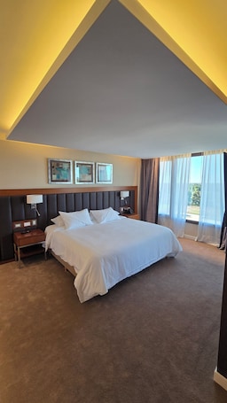 A hotel room with a large bed, a nightstand, a lamp, a phone, and a window with curtains.. Azahar Hotel & Spa