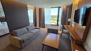 Une chambre d’hôtel équipée d’un canapé, d’un pouf, d’une table basse, d’une télévision et d’un lit.