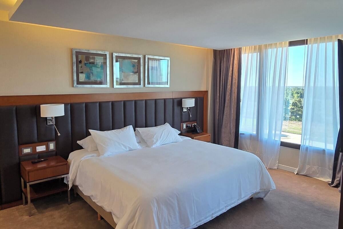 Una habitación de hotel con una cama grande, una mesita de noche, una lámpara, un teléfono y una ventana con cortinas.