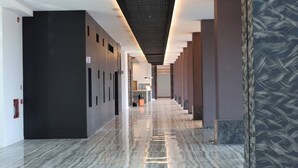 Un pasillo moderno de hotel con piso de mármol, paredes oscuras y un diseño decorativo en la pared derecha.