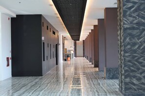Moderni hotellikäytävä, jossa on marmorilattia, tummat seinät ja oikealla puolella kuvioitu seinä.