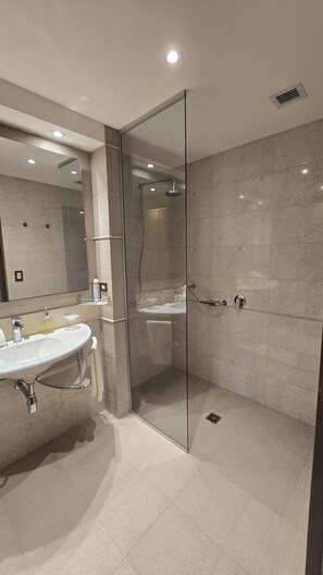 A modern bathroom with a glass-enclosed shower, a sink with a mirror, and a tiled floor.