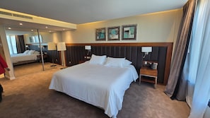 Une chambre d’hôtel avec un grand lit, des tables de chevet, un miroir et des œuvres d’art accrochées au mur.