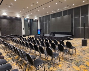 A conference room with rows of chairs, a stage, a large screen, and a podium.
