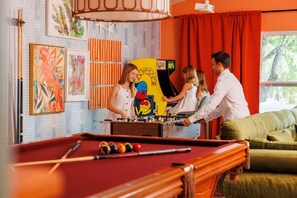 A pool table with a foosball table in a room with red curtains and artwork on the walls. - Pool, Hot Tub, PickleBall, Firepit, 5 min to IMG (Bradenton)