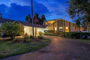 A two-story house with a driveway leading to a garage, surrounded by greenery and palm trees. - Pool, Hot Tub, PickleBall, Firepit, 5 min to IMG (Bradenton)