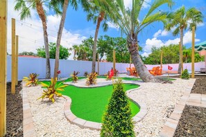 A landscaped garden with palm trees, a small pond, and orange chairs. - Pool, Hot Tub, PickleBall, Firepit, 5 min to IMG (Bradenton)