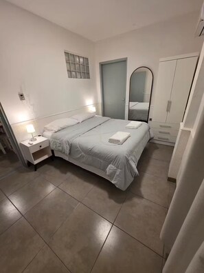 Ein Schlafzimmer mit Bett, Nachttisch, Spiegel, Kleiderschrank und einer Tür.