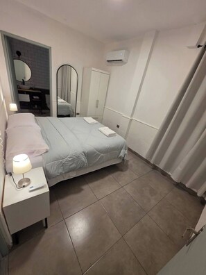 Un dormitorio con cama, mesita de noche, lámpara, espejo, armario y equipo de aire acondicionado.