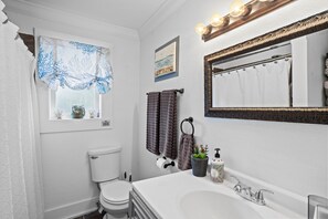 A bathroom with a toilet, sink, mirror, and towel rack. - Magnolia Beach Cottage (Gulfport)