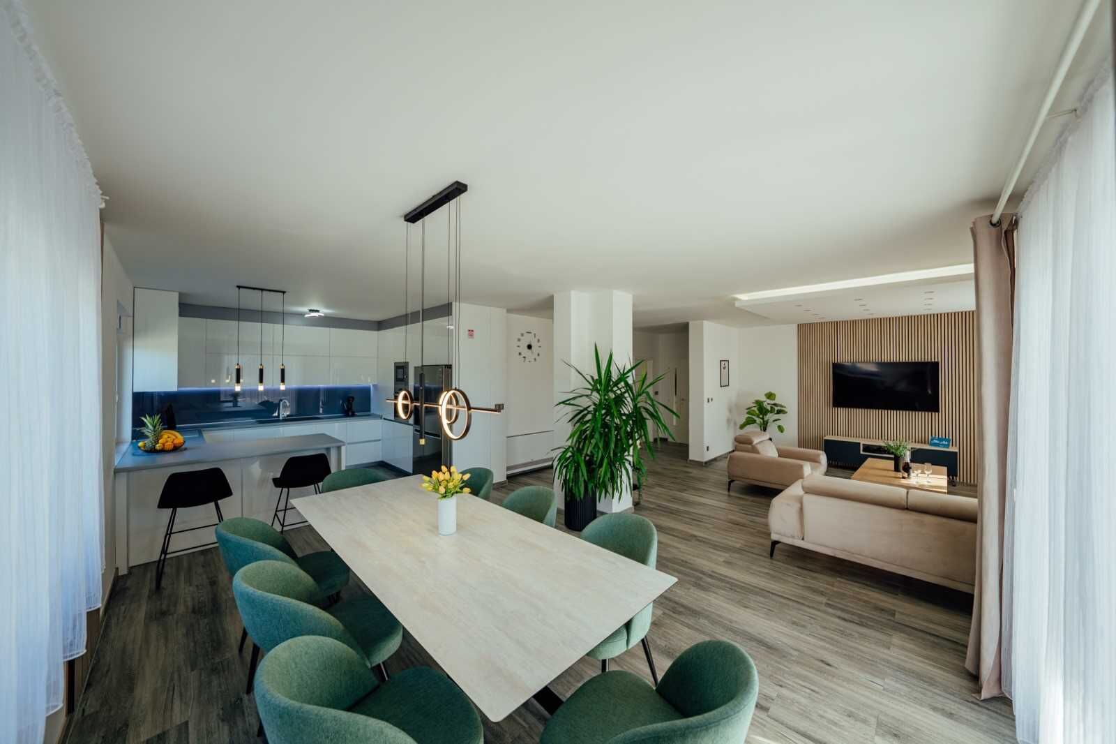A modern apartment with a dining area, kitchen, living room, and a TV mounted on the wall.