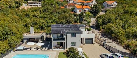 A modern two-story house with a swimming pool, solar panels, and a garage.