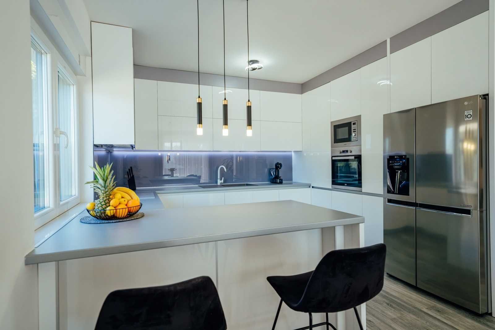 A modern kitchen with a central island, stainless steel appliances, and black chairs.